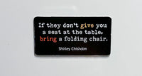 Picture of two by three inch black rectangular fridge magnet with quote by Shirley Chisholm reading "If they don't give you a seat at the table, bring a folding chair".