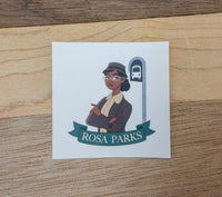 On white sticker paper, close-up of image of cartoon illustrated Rosa Parks wearing a brown twill blazer and yellow club-collar blouse. She stares confidently through silver-rimmed glasses with a brown trilby style hat on her dark brown hair. She is standing in front of a bus stop sign in the background. Below her image is a dark green ribbon with her name in light yellow typeface. Sticker measures 2 by 2 inches in area.    